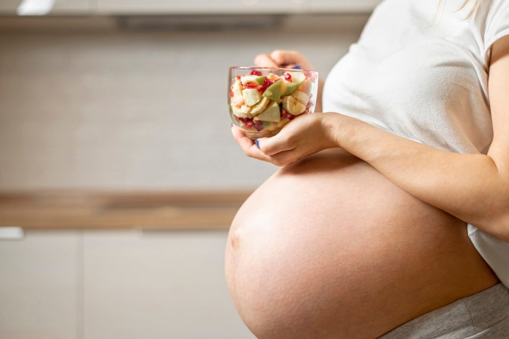 Mulher grávida segurando um pote com frutas